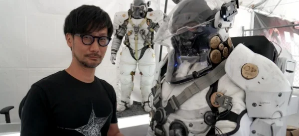 Imagem mostra Hideo Kojima ao lado de uma estátua em tamanho humano do robô símbolo do estúdio Kojima Productions